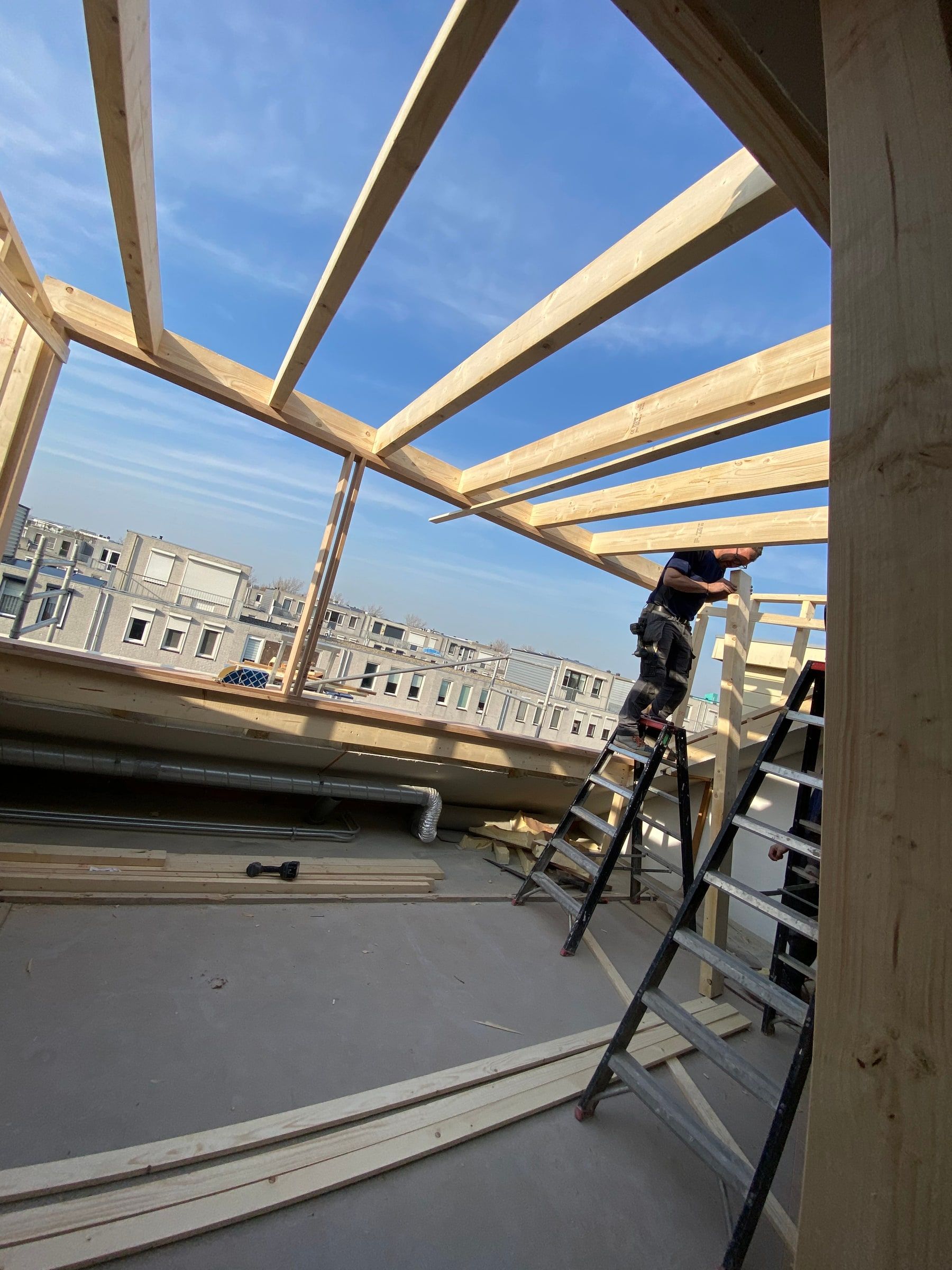 Houten spanten van een dakopbouw in aanbouw, tegen een blauwe lucht
